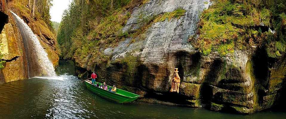 Boat gliding through a narrow sandstone gorge with forest reflections
