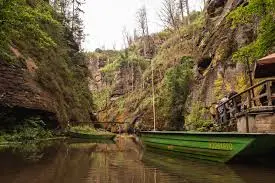Boat gliding through a narrow sandstone gorge with forest reflections